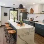 Kitchen with marble seated island and chairs, blue cabinets, and brown wood floors